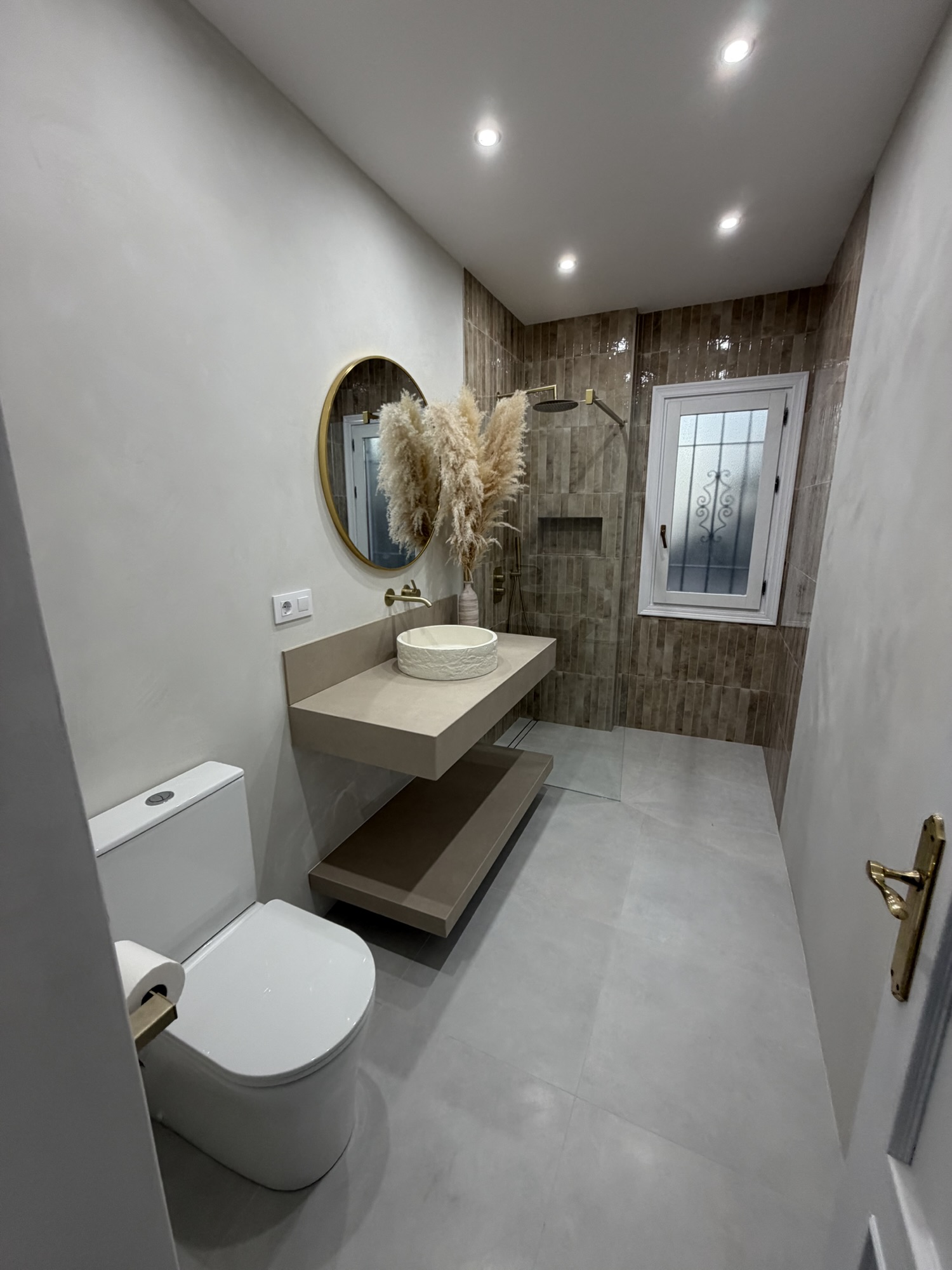 Baño con lavabo sobre encimera, espejo ovalado y zona de ducha revestida.