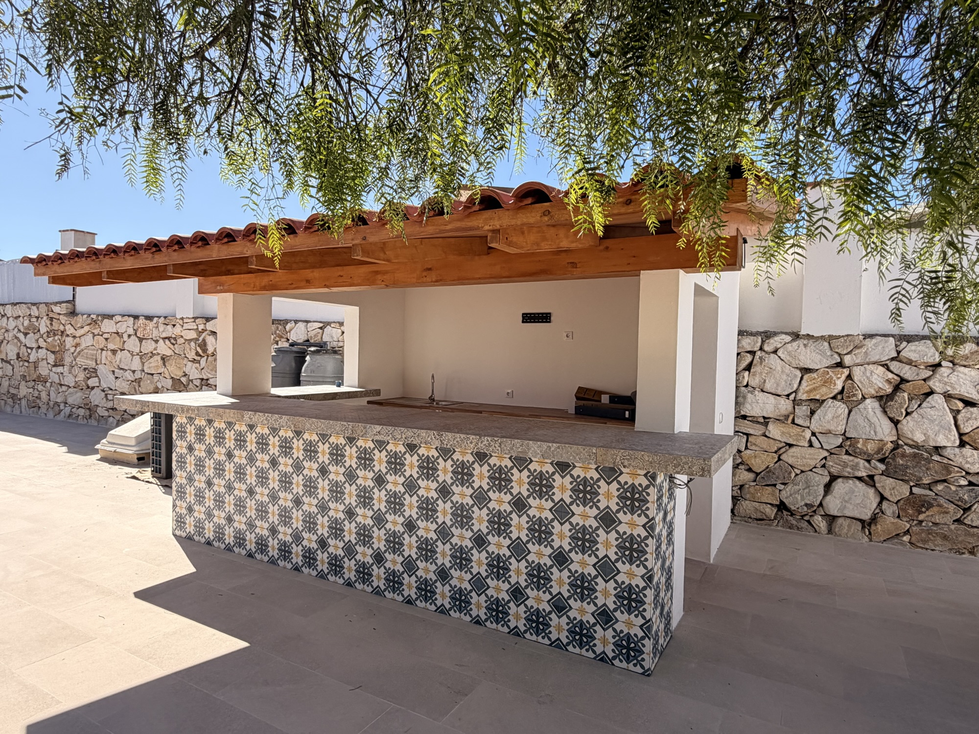 Cocina exterior con barra de azulejos decorativos y cubierta de madera y teja.